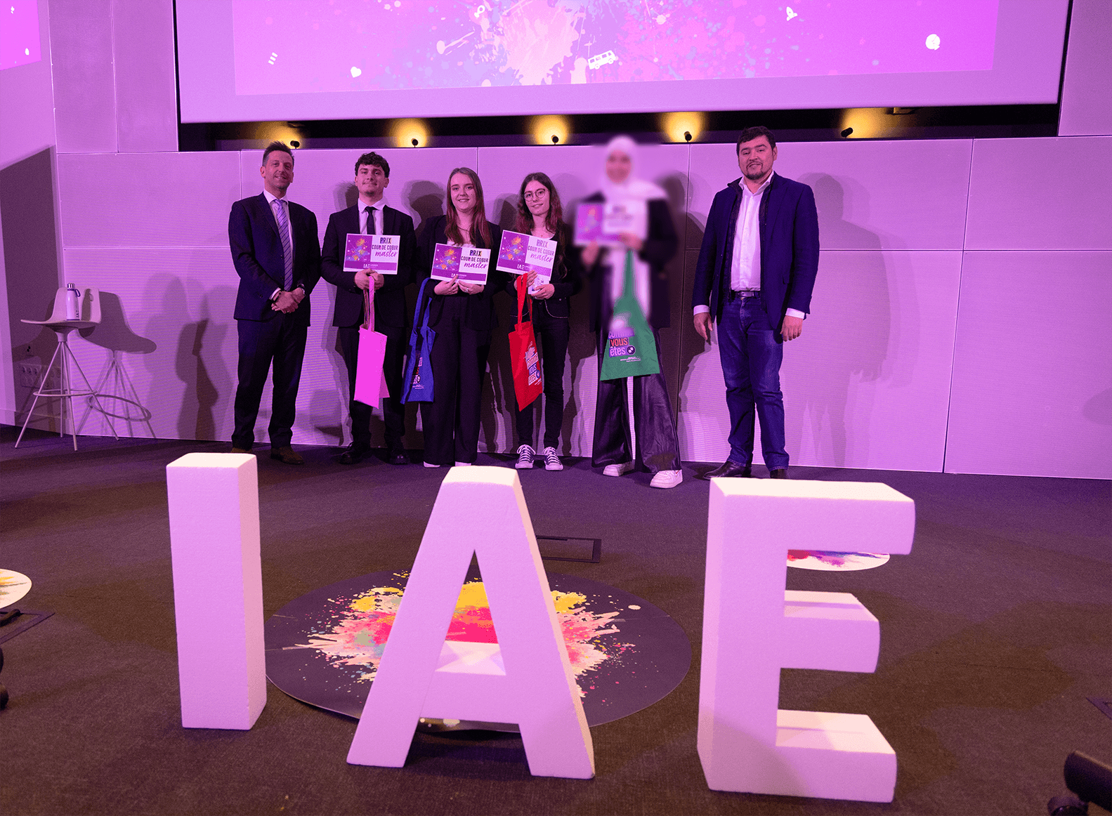 Remise de prix lors de la finale 2025 des Ateliers de l’innovation de l'IAE Limoges. Lauréats et membres du jury sont alignés sur scène, tenant diplômes et trophées, devant de grandes lettres formant « IAE ». L'événement met en lumière les projets innovants des étudiants.